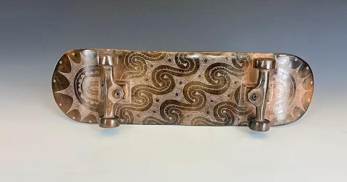 A skateboard with ceramic wheels and deck, featuring intricate, swirling patterns and designs engraved on the surface, displayed against a neutral gray background.