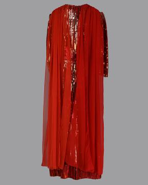 A floor-length, shimmering red dress with sequins and a sheer red overlay, displayed against a plain gray background. The dress features long sleeves and a flowing, elegant design.