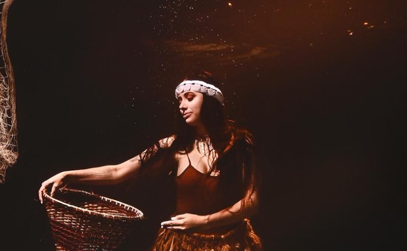 An Indigenous American women under water holding a basket