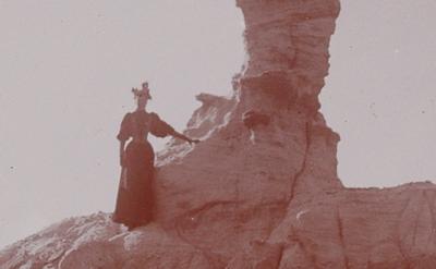 woman in late 1800s dress standing on rock formation