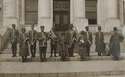 black and white photograph of an all-Black musical band on the steps of a courthouse, carrying various instruments