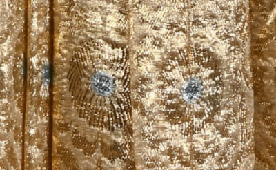 Golden fabric with shimmering, intricate patterns and silver floral motifs. The texture and metallic sheen give it an elegant appearance.