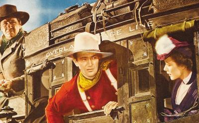 Three people in Old West attire ride a stagecoach. A man in a white hat and red shirt looks ahead, a woman in a purple dress peers out the window, and a driver sits on top, holding the reins. The coach reads “Overland Stage Line.”.