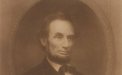 Sepia-toned portrait of Abraham Lincoln, shown from the chest up, facing slightly to the side, wearing a dark suit, white shirt, and bow tie, with a somber expression inside an ornate oval frame.