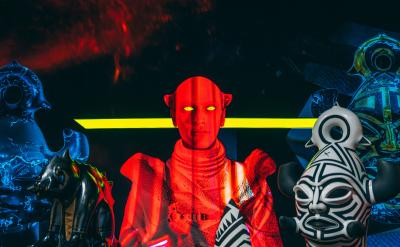 Red person with yellow eyes yellow line behind him, bottom right bust in black and white, other figures in black background