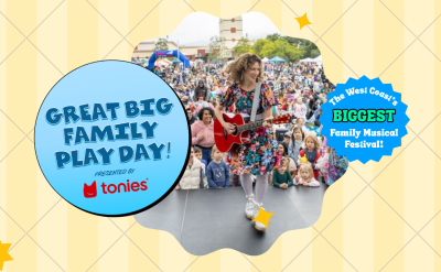 A woman in a floral dress plays guitar and sings on an outdoor stage, entertaining a large audience of families at the Great Big Family Play Day festival, presented by Tonies. Banners announce it as the West Coast’s biggest family musical festival.