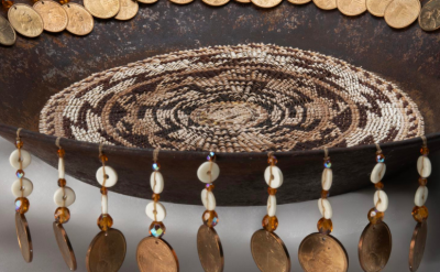 A shallow, round bowl with beaded decoration on the inside and a hanging fringe of coins, beads, and shells around the rim.