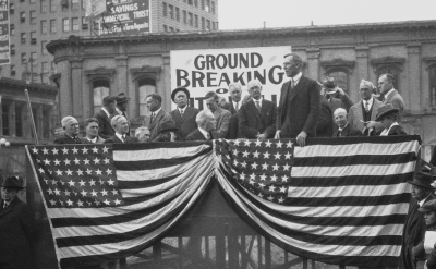A black-and-white photo of a groundbreaking ceremony with people and an American flag, next to a color photo of a tall government building with palm trees in front.