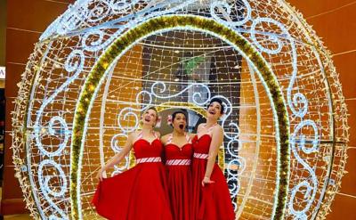 Three singers in red dresses performing inside a large, illuminated spherical holiday ornament.