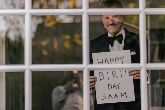 a man in a tuxedo behind a window with a happy birthday sign