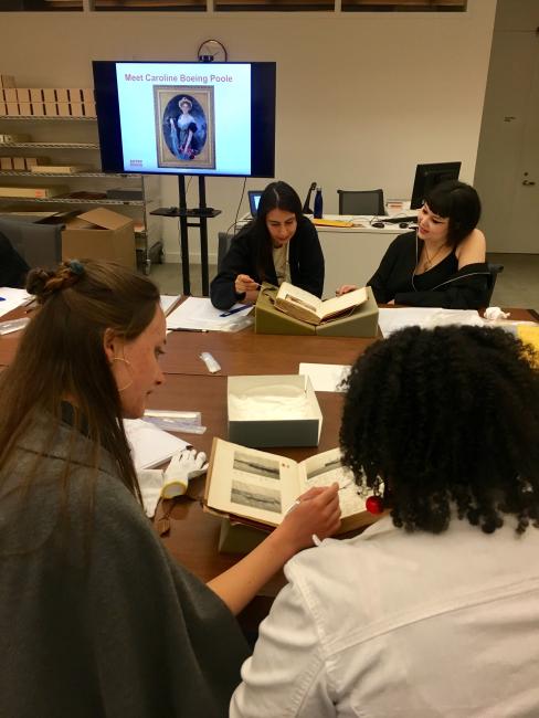 students and library desks examining archival materials TV monitor with still image of a painting in background