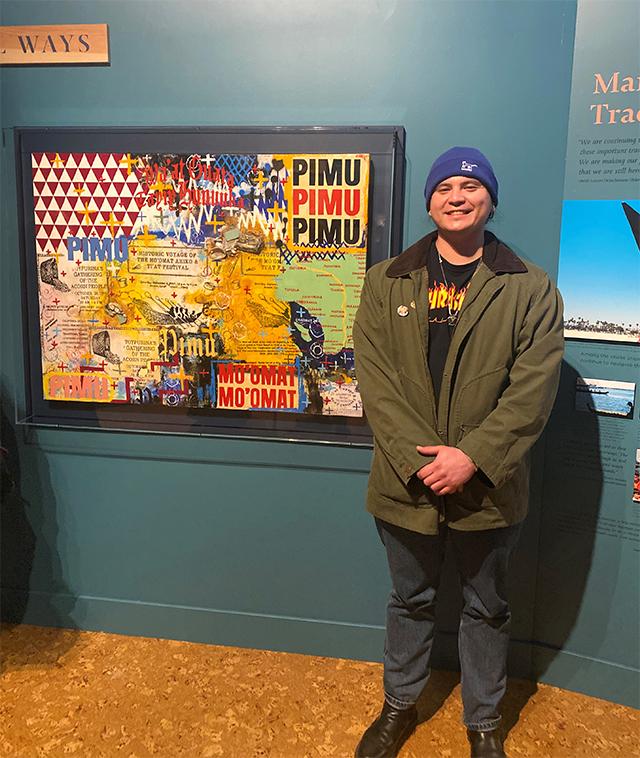 a man in a jacket and beanie stands beside a collage artwork