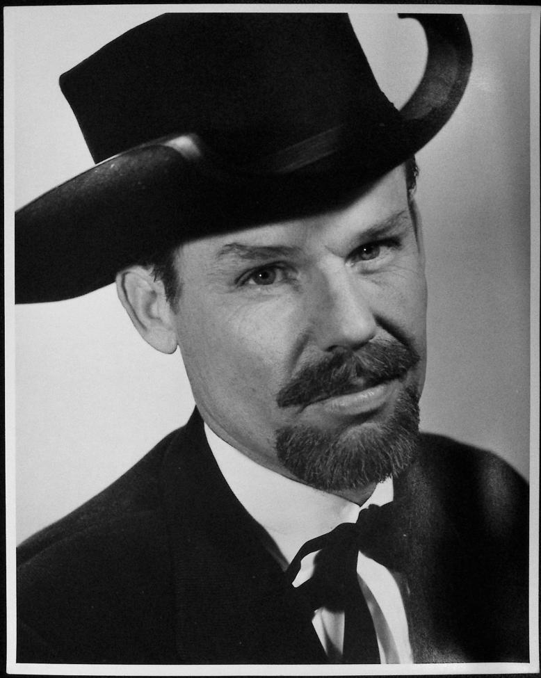 Black-and-white portrait of a man wearing a suit, a bowtie, and a wide-brimmed hat with upturned sides. He has a goatee and mustache, and is looking slightly to the side with a neutral expression.