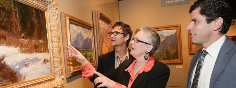 3 people looking at a painting of a landscape