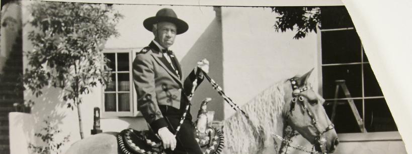 black and white photograph of a man riding a horse, with the reins in his left hand