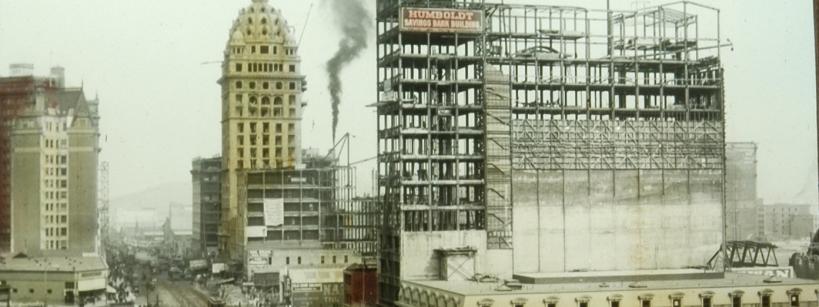 buildings being constructed, with a plume of industrial smoke in the background