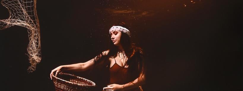 An Indigenous American women under water holding a basket