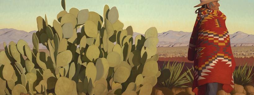 A person wearing a wide-brimmed hat and a colorful patterned blanket stands next to a large cactus in a desert landscape with mountains in the distance under a clear sky.