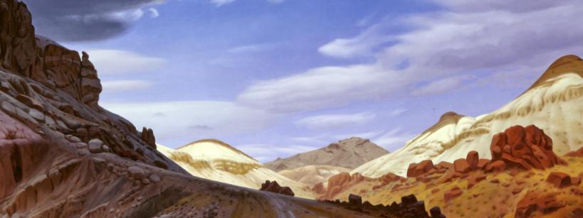 A wide desert landscape with rocky hills, golden sand dunes, scattered red boulders, and a partly cloudy blue sky.