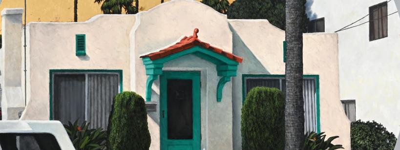 A small white stucco house with a red-tiled roof and teal trim on the door and windows, surrounded by neatly trimmed bushes, palm trees, and a partial view of a white vehicle in the foreground.
