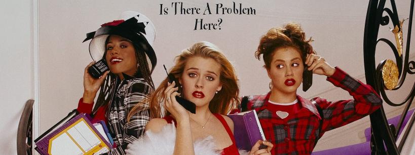 Three young women in 1990s fashion hold large cell phones and planners, standing on a staircase. Above them, text reads “Is There A Problem Here?” They look surprised or concerned.