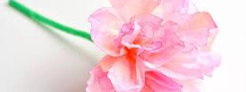 A close-up of a delicate, pink paper flower with a green stem, displayed against a white background.