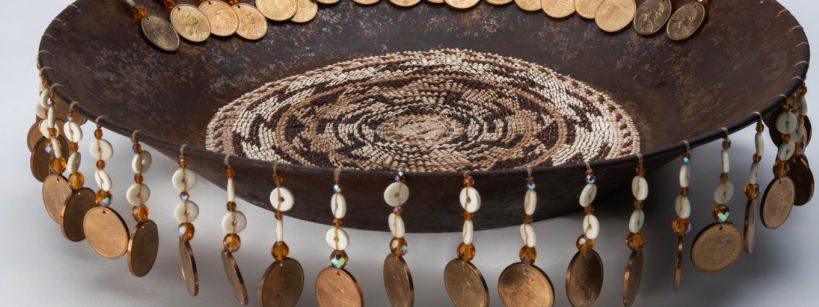 A shallow, round bowl with beaded decoration on the inside and a hanging fringe of coins, beads, and shells around the rim.