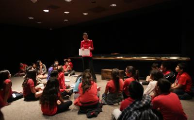 museum teacher standing with students sitting in a circle around her