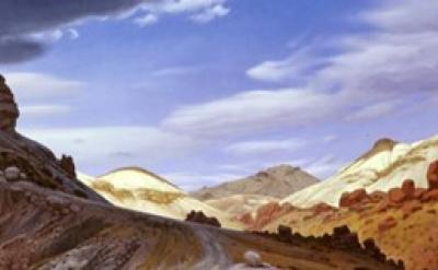A winding dirt road curves through a rocky desert landscape with reddish and tan hills under a partly cloudy blue sky.