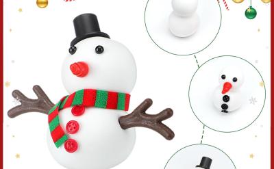Step-by-step guide showing how to make a snowman craft with a scarf, buttons, hat, carrot nose, and stick arms, set against a festive background with ornaments and Santa in a sleigh.