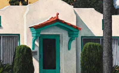 A small white stucco house with a red tile roof and green trim on the door and windows, surrounded by bushes and palm trees, with part of a white car visible on the left.