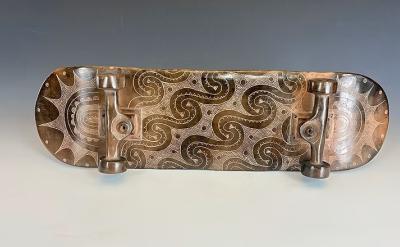 A skateboard with ceramic wheels and deck, featuring intricate, swirling patterns and designs engraved on the surface, displayed against a neutral gray background.