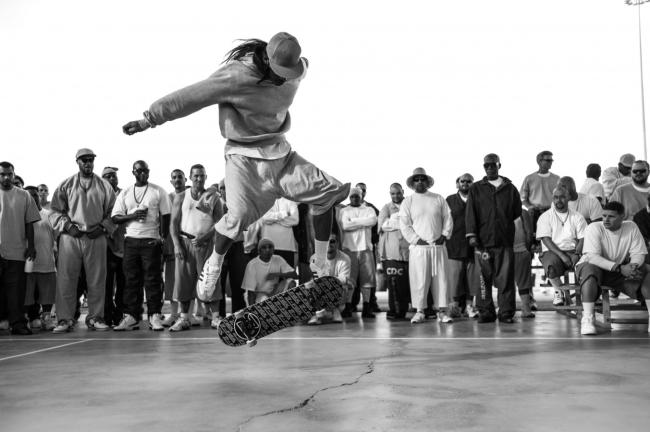 a prisoner skateboards, a group of prisoners watch