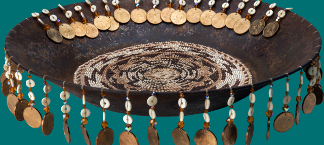 A decorative bowl with intricate beadwork inside and a rim adorned with hanging coins, shells, and beads, set against a teal background.