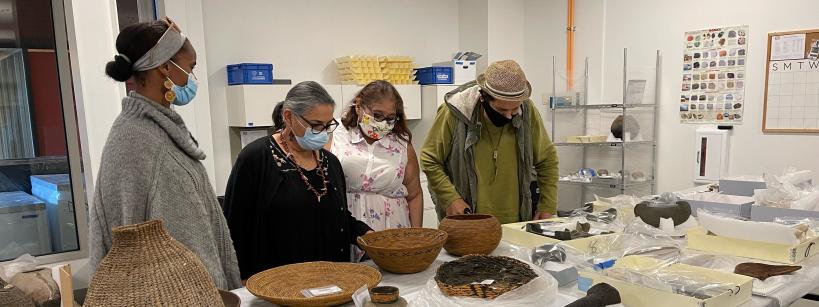 four people stand around a table examining items laid out on the table