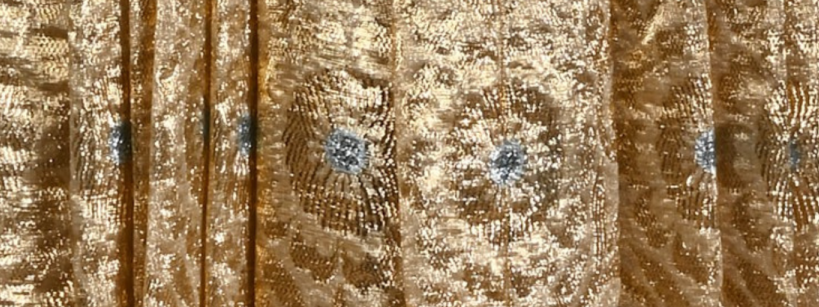 Golden fabric with shimmering, intricate patterns and silver floral motifs. The texture and metallic sheen give it an elegant appearance.