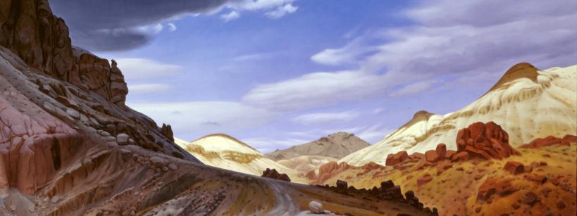 A dramatic desert landscape with rocky hills, reddish and tan earth, winding paths, and a sky filled with large, swirling clouds under bright blue.